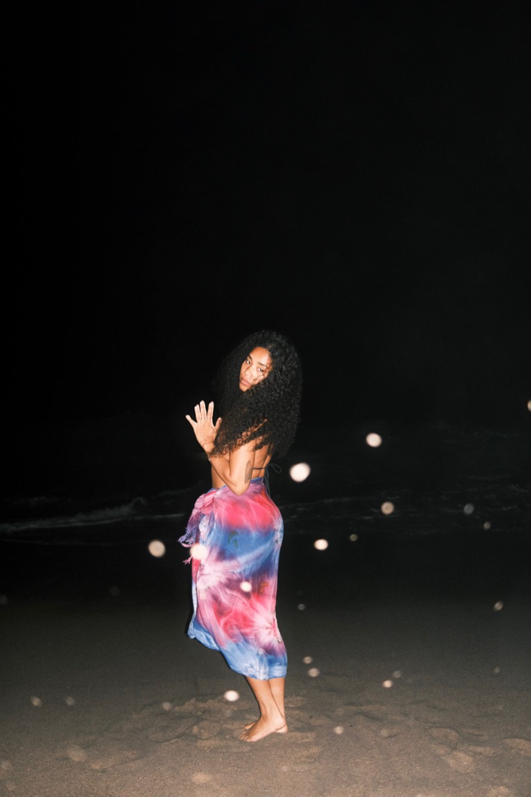 Kayla on the beach at night, barefoot in the sand, wearing a magenta and cobalt tie-dye wrap